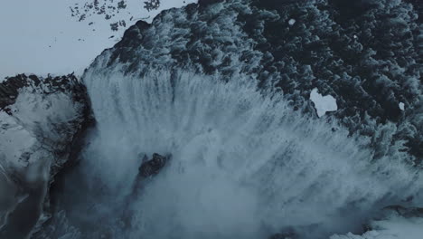 icelandic waterfall in winter season, birdseye aerial view of glacial water and snowy landscape