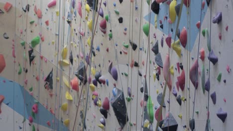 Indoor-rock-climbing-wall-with-colorful-holds-and-ropes