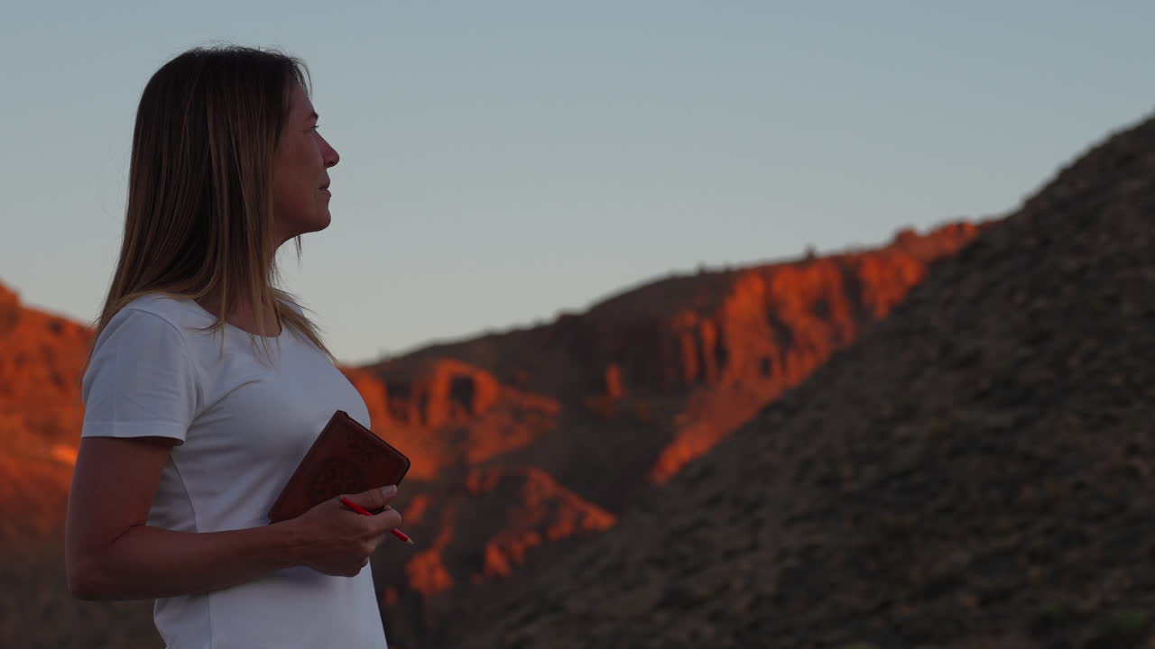 Woman holding a notebook and a pen, admiring the sunset over the Teide volcano in Tenerife, Canary Islands