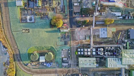 overhead aerial footage of a large industrial plant showing pipework structures, buildings, cooling towers, steam, and work vehicles