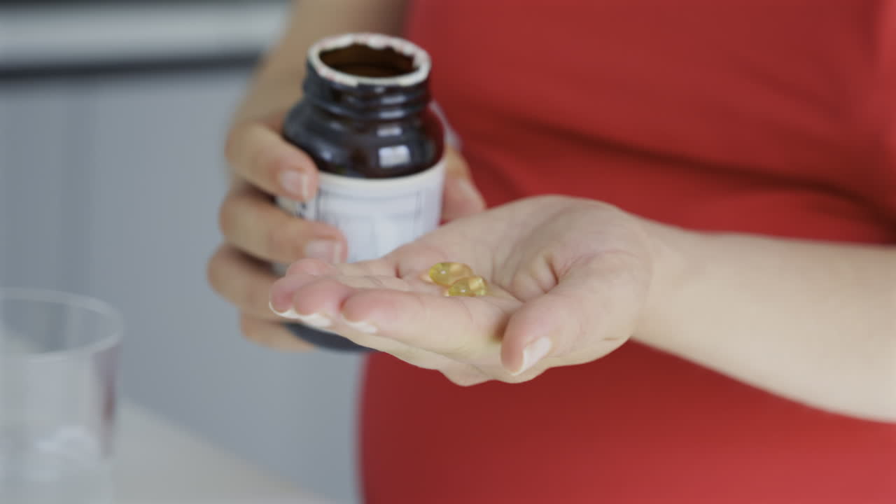 Close up of a pregnant woman pouring fish oil supplements out of into her palm