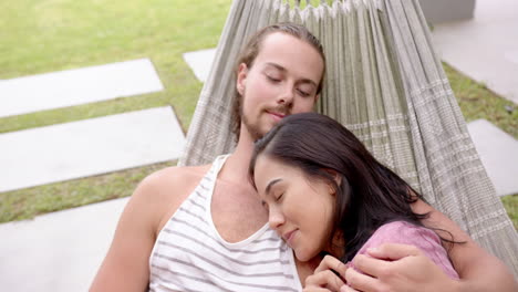 a young diverse couple relaxes in a hammock in the backyard at home