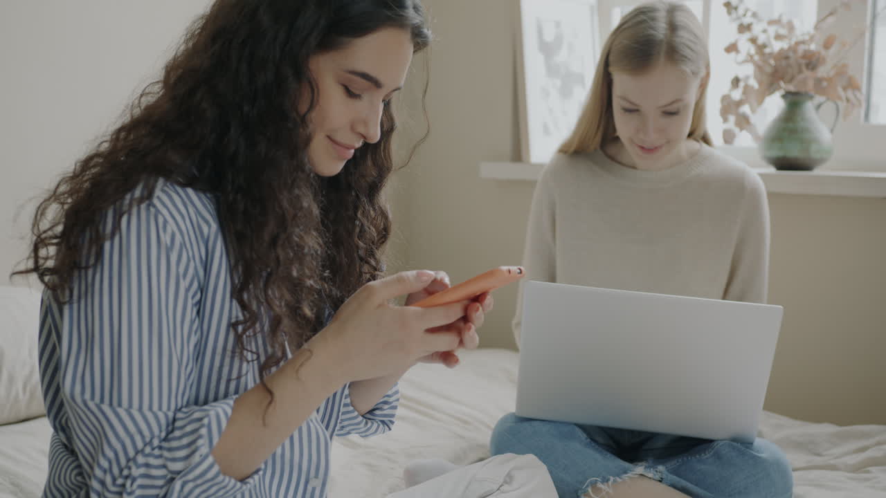Two Young Women Using Phones and a Laptop