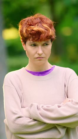 portrait of a serious redhead woman with crossed arms outdoors