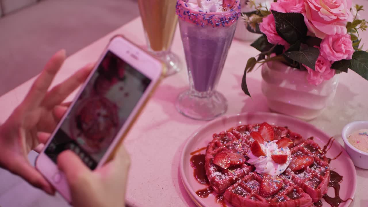 hermosa mujer tomando varias fotos de su colorido waffle y taro frappe para instagram en una cafetería de temática rosa