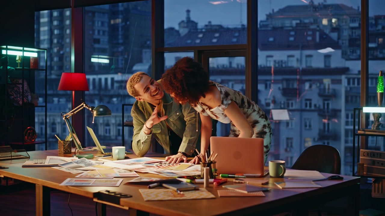 Two designers discussing color palette samples in evening office studio