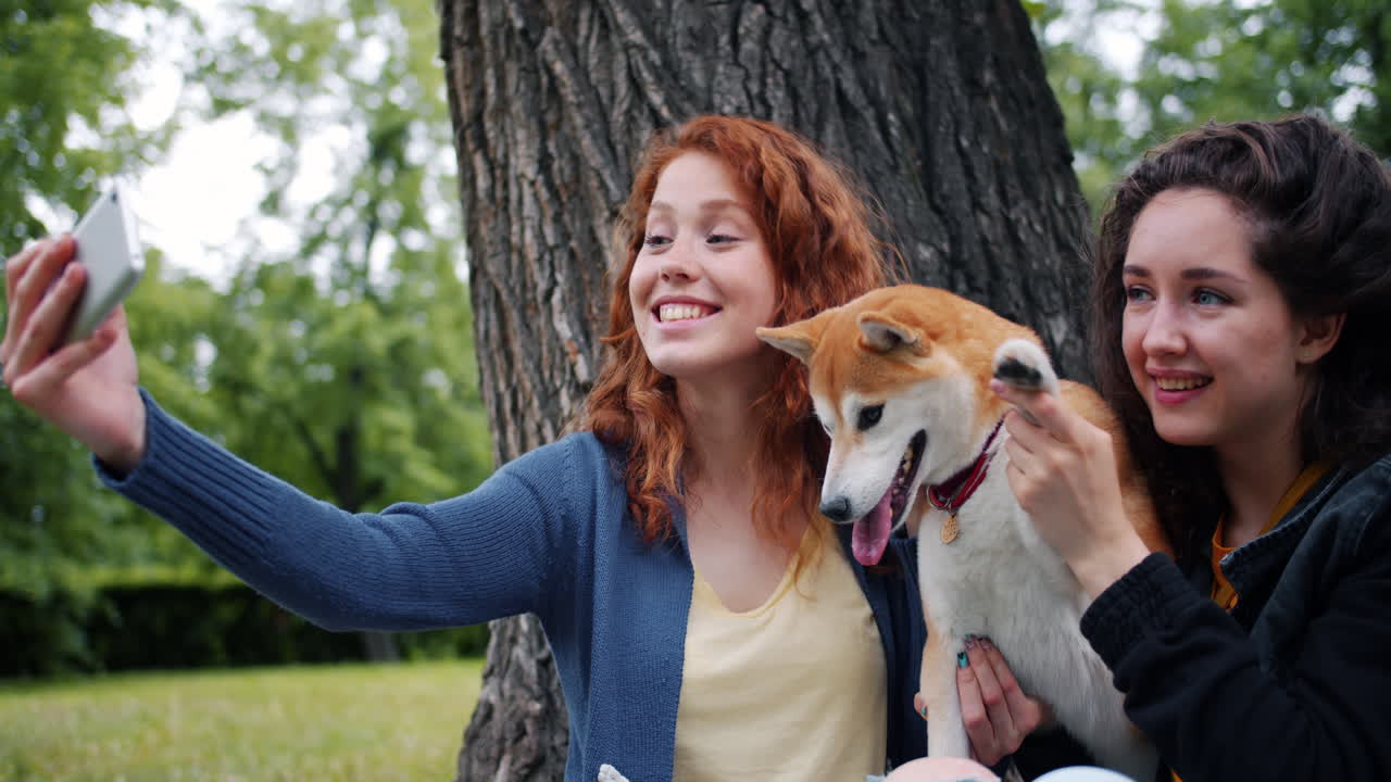 Two girls taking a selfie with a Shiba Inu dog in a park