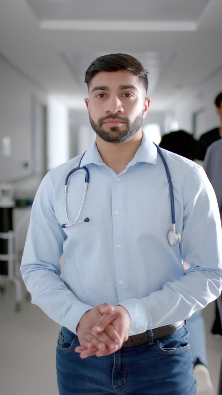 Video vertical de retrato de un médico birracial feliz en el pasillo del hospital, a cámara lenta.