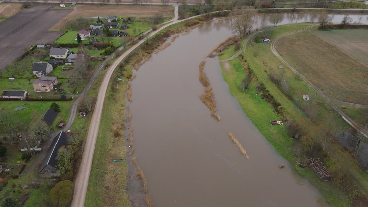 Aerial establishing view of high water in springtime, Barta river flood, brown and muddy water, overcast day, wide birdseye drone shot moving forward
