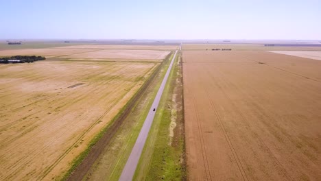 aerial view of vehicle on country road driving through farmland at daytime - drone shot
