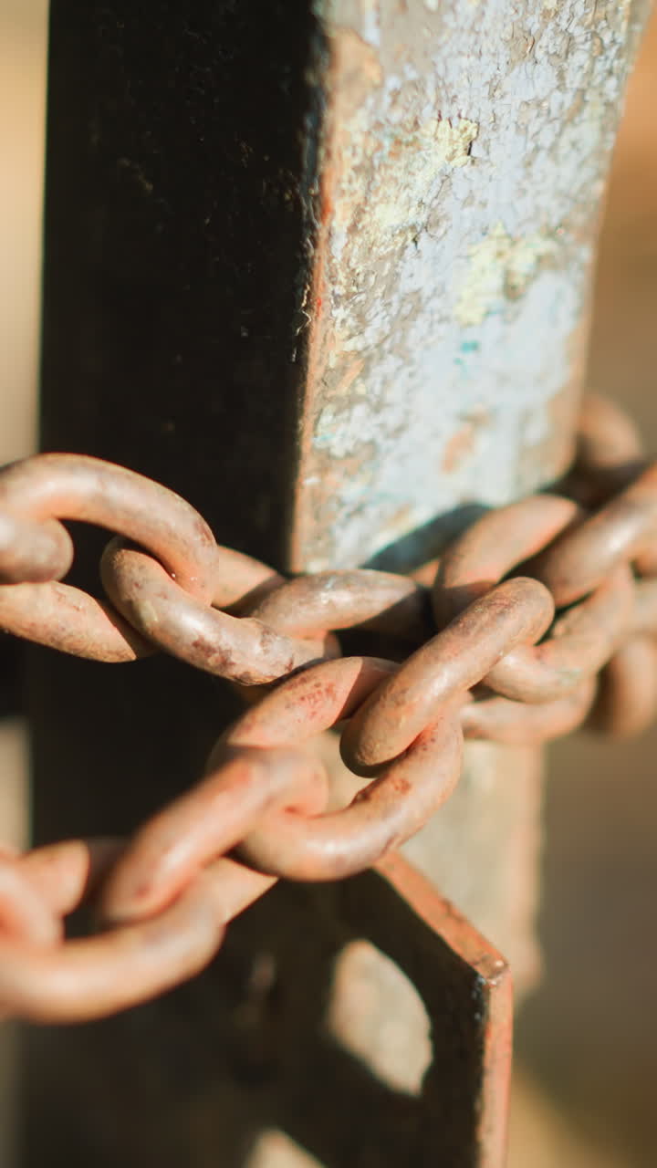 primer plano de una cadena oxidada enrollada alrededor de un poste metálico que muestra corrosión y pátina, la luz del sol destaca la textura rugosa y el grano, una puerta industrial que transmite seguridad y abandono, eslabones pesados que sugieren