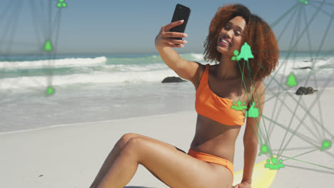 animation of networks with digital icons over woman taking selfie with smartphone on beach