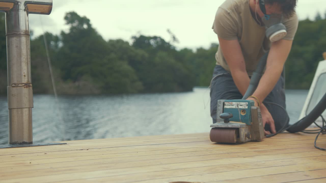 Carpenter sanding roof of wooden boat using belt sander