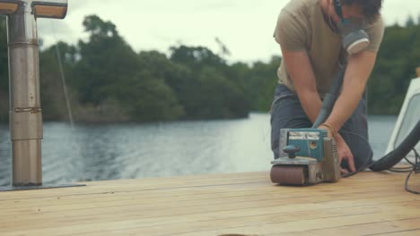 Carpenter-sanding-roof-of-wooden-boat-using-belt-sander