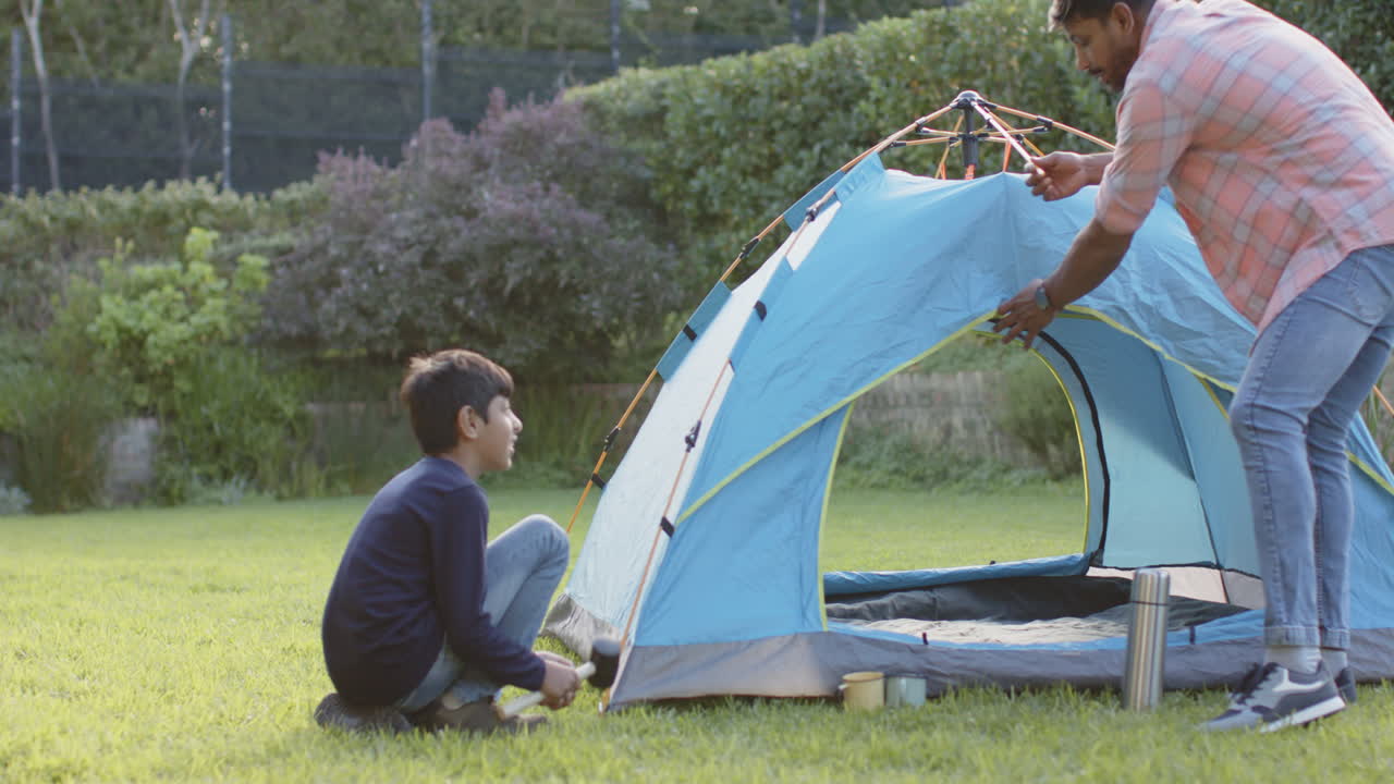 Setting up blue tent, Indian father and young son camping together outdoors