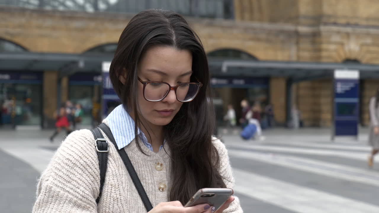 Beautiful Asian American Woman stood outside Kings Cross Station, London using her smartphone