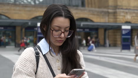 hermosa mujer asiática americana se paró afuera de la estación de kings cross, londres usando su teléfono inteligente