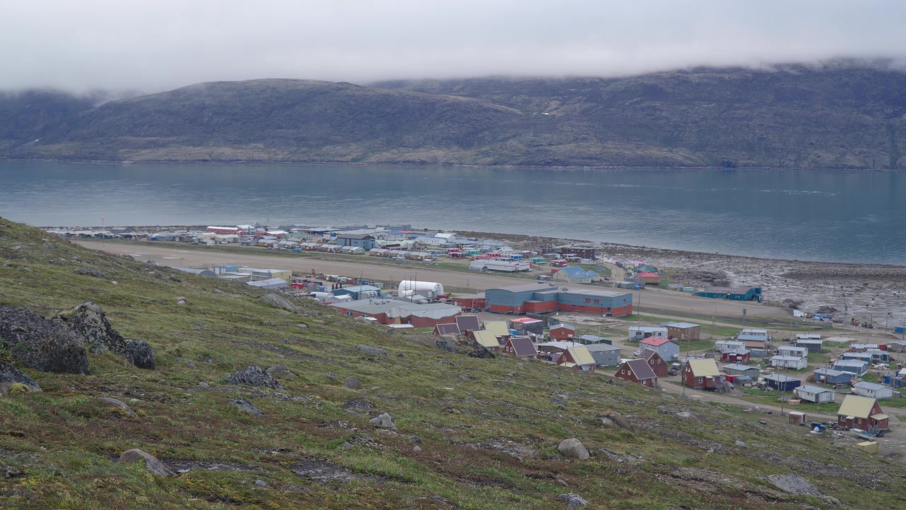 Ampia prospettiva elevata che si affaccia sulla pista di atterraggio in ghiaia, sulle abitazioni comunali e sullo sfondo montuoso di Pangnirtung, Nunavut