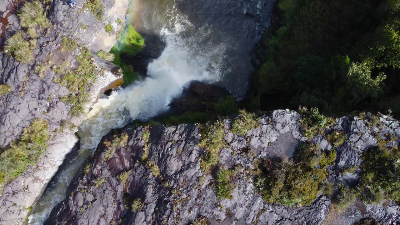 A stunning aerial pan shot capturing the powerful flow of Fuego Waterfall near Cotopaxi, Ecuador. The rushing water cascades down rugged volcanic rocks, creating a breathtaking natural spectacle.