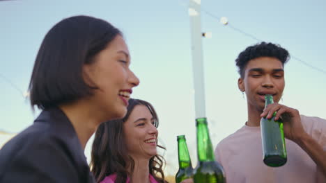 amigos multiétnicos bebiendo cerveza en un primer plano en el techo. gente despreocupada brindando