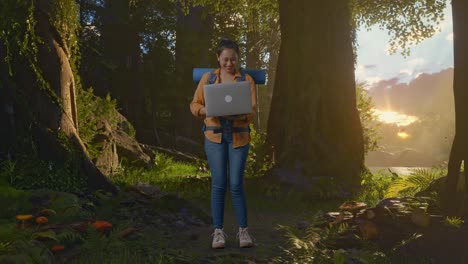 cuerpo lleno de excursionista femenina asiática con mochila de montañismo usando una computadora portátil mientras explora la naturaleza del bosque