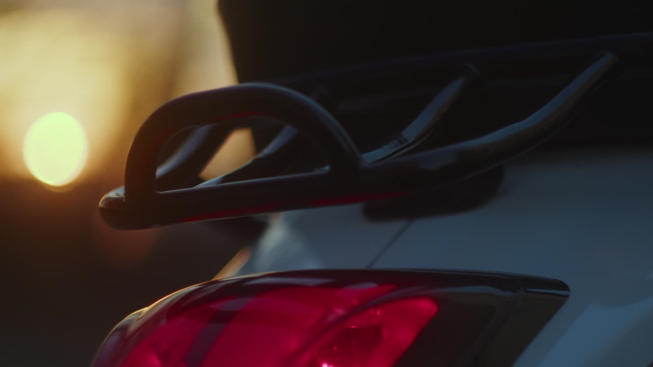 Close-up of a scooter's tail light and rear rack at sunset