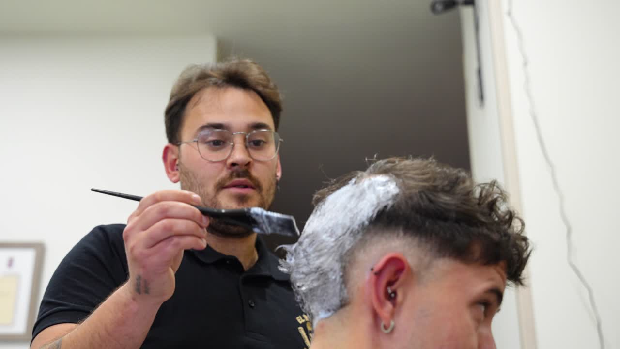 Joyful hairdresser and client share laughter during bleaching process. Rack focus