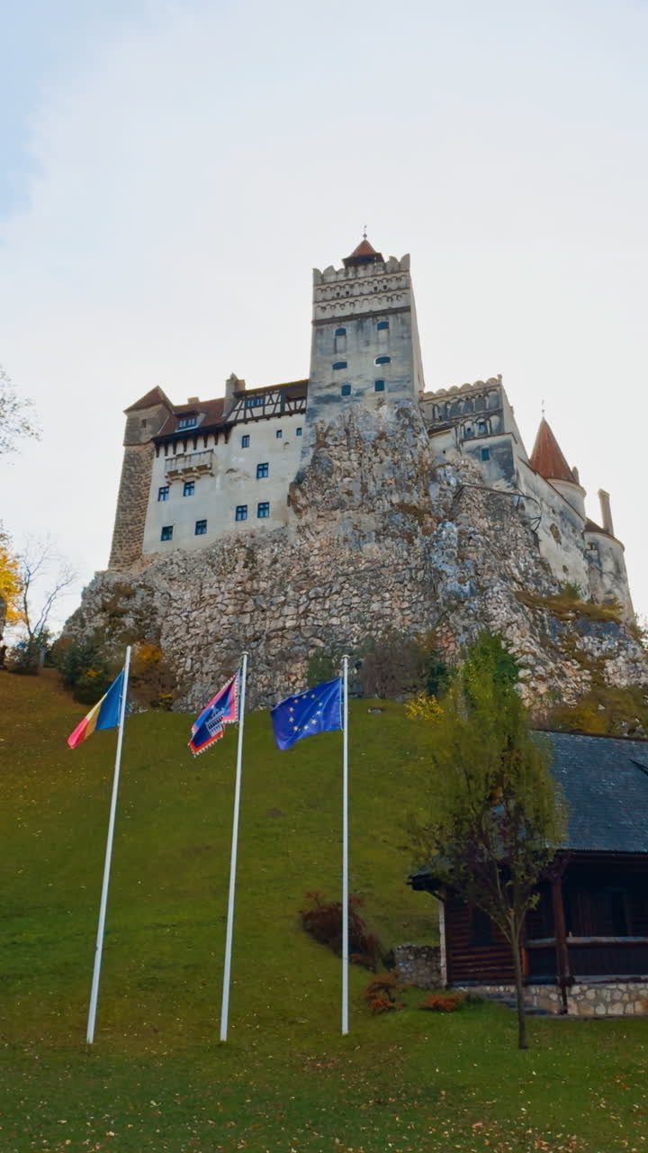 Beautiful view of old castle standing on the hill among the autumn nature. Low angle view on the Bran castle, Romania on Halloween season. Vertical video