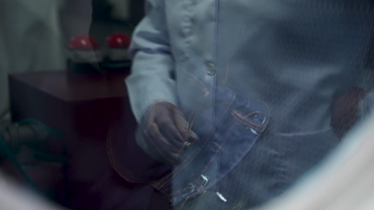 Reflejo de un científico en el cristal de una máquina mientras prueba textiles en busca de productos químicos en un experimento.
