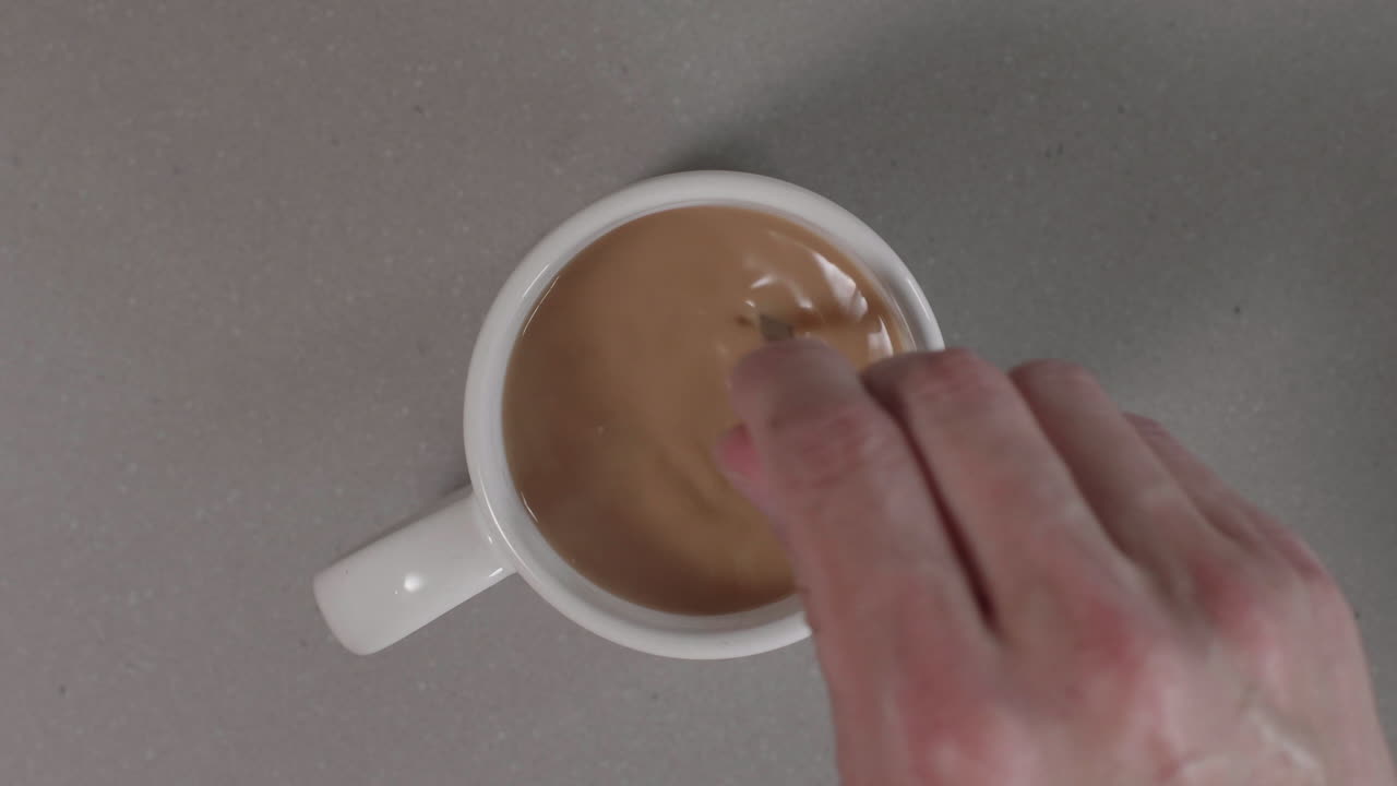 Stirring a mug of coffee with cream and sugar in slow motion ( 60fps ) from a birds eye view, 4K.