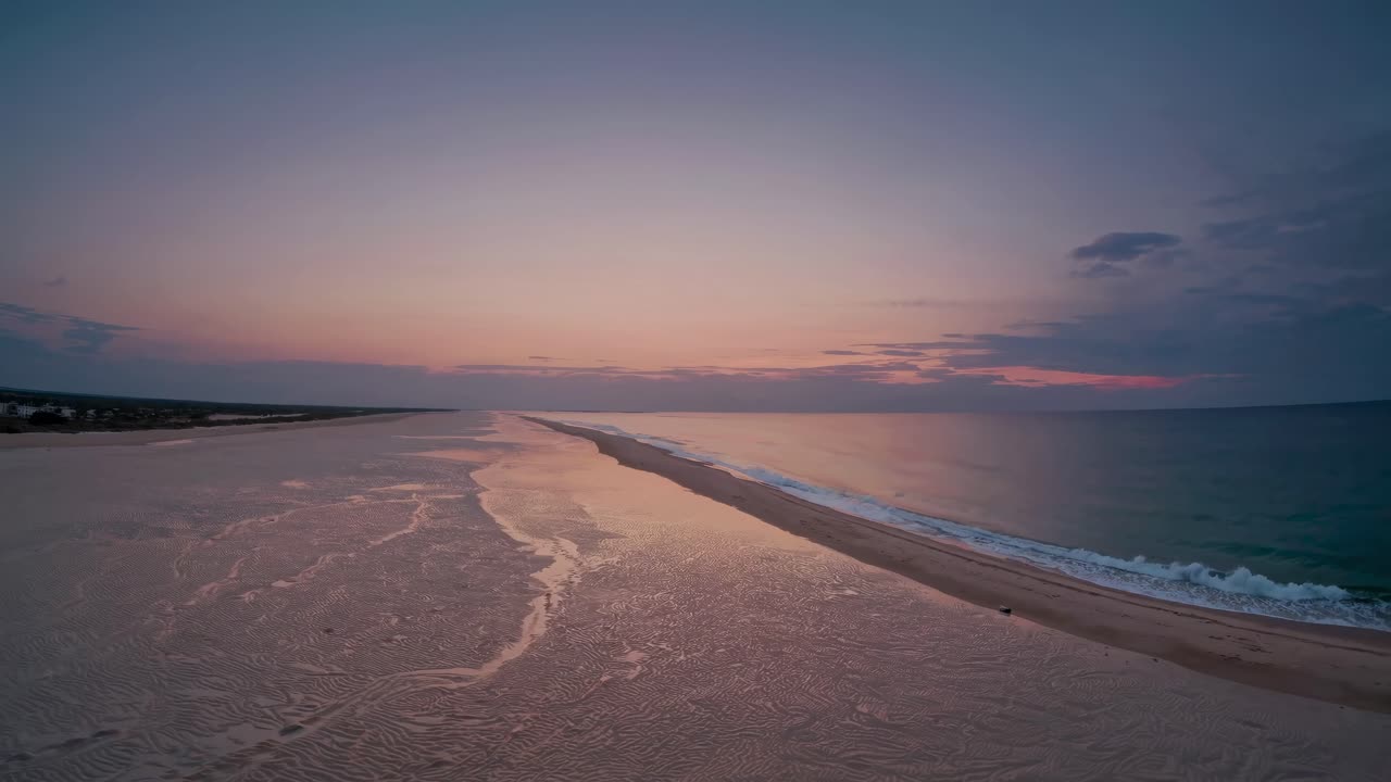 Aerial video captures a serene beach at sunset, showcasing the tranquil meeting of sand and sea