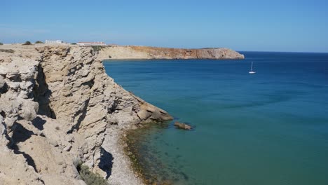 Establishing-shot,-Scenic-view-of-Rocky-cliff-in-Algarve,-Portugal,-boat-floating-in-the-sea-on-a-bright-sunny-day