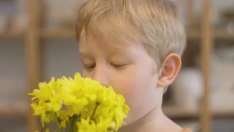 Nahaufnahme-Eines-Blonden-Kindes,-Das-Gelbe-Blumen-Riecht-Und-In-Einer-Handwerkswerkstatt-In-Die-Kamera-Schaut-1