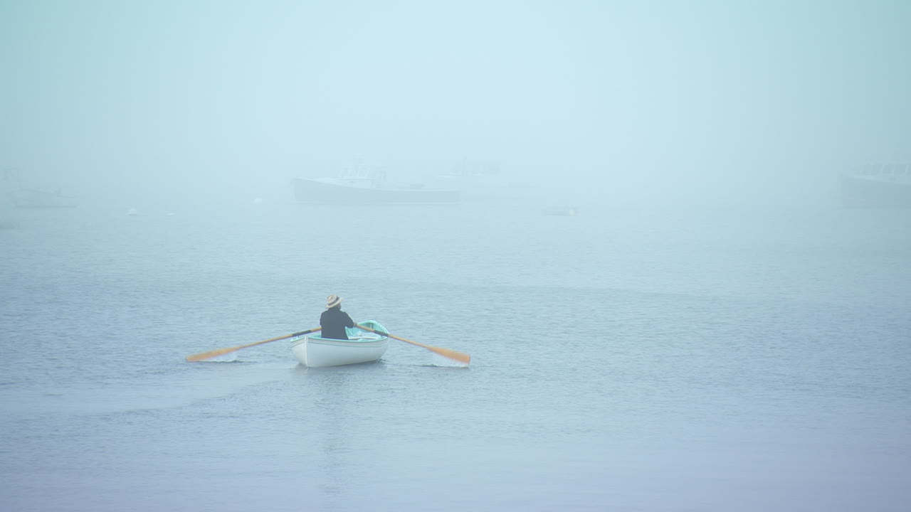 Closeup of man rowing a row boat into the eerie Maine fog.