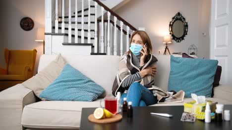 sick woman wearing a medical mask sitting on the sofa and talking on cellphone