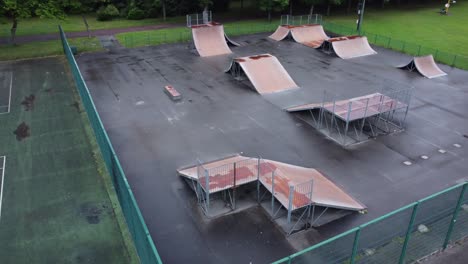 Aerial-view-flying-above-fenced-skate-park-ramp-in-empty-closed-playground-tilting-down