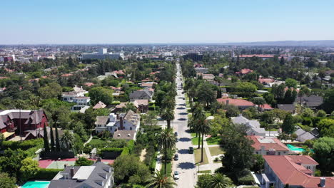 drone flies over palm tree and mansion lined street with white car driving down in beautiful west hollywood, los anf