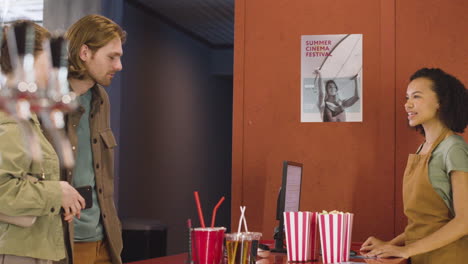 smiling female clerk selling movie tickets to a couple and the woman paying with phone