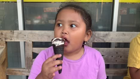 Niña-Asiática-Lamiendo-Helado-Grande-En-Cono-De-Gofres-Con-Chocolate-Frente-Al-Mercado