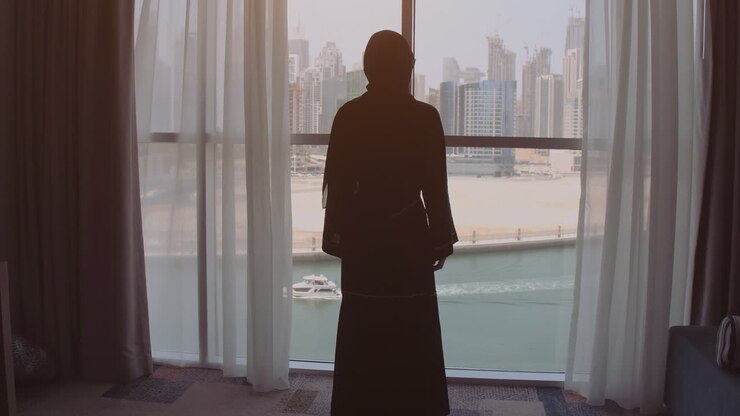 mulher em abaya olhando pela janela do hotel
