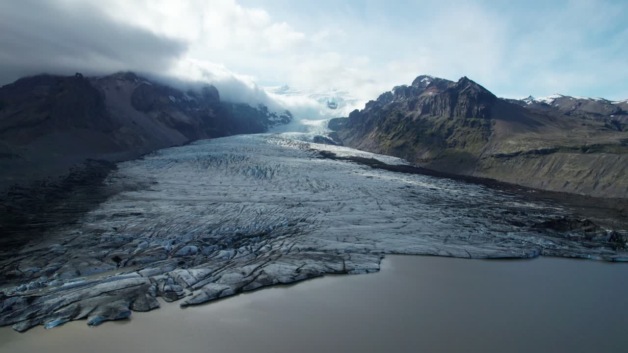 vista aérea del glaciar vatnajökull rodeado de nubes y montañas durante el verano en islandia, mostrando su inmensa escala y el paisaje dramático