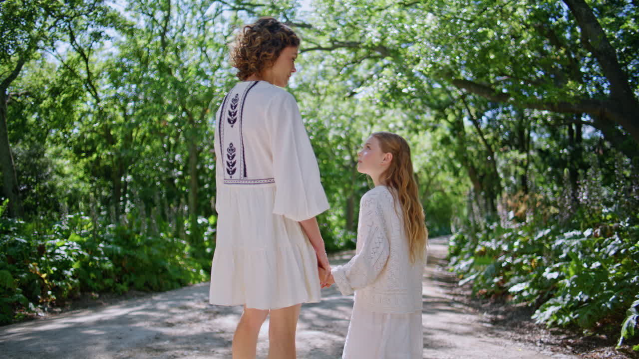 Mother daughter stepping sunny garden at weekend back view. Woman girl walking
