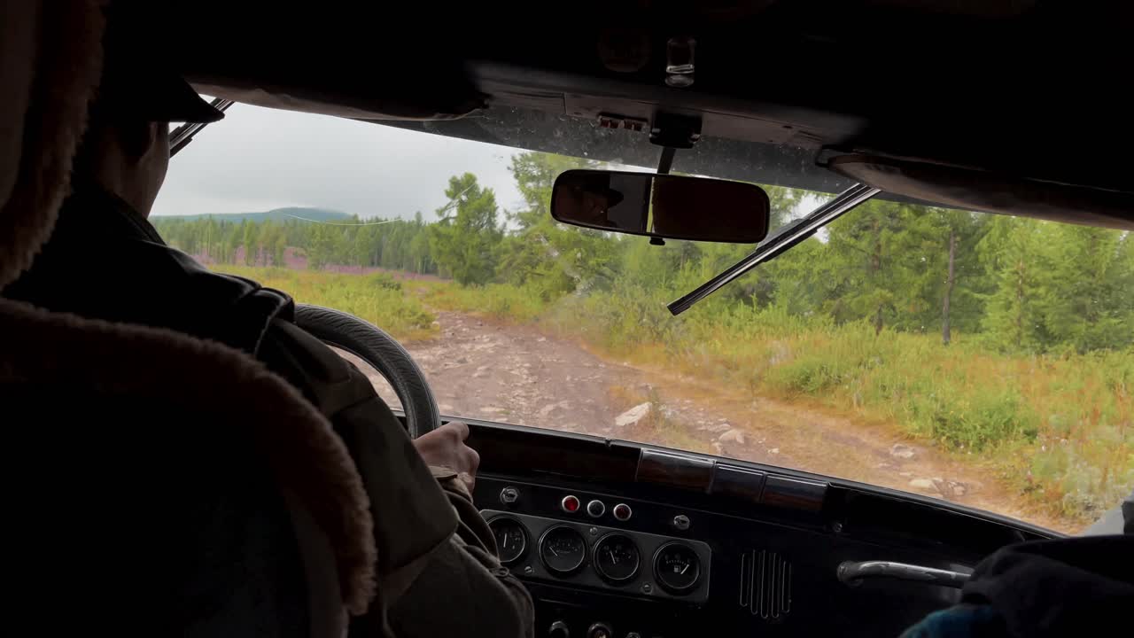 ロシアのアルタイ地方。緑の森と畑の中を泥だらけの未舗装路を車で走る車内からの視点。旅行と冒険のコンセプト、夏の田園風景。