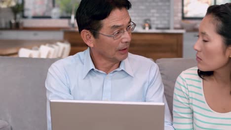 asian couple using laptop on sofa