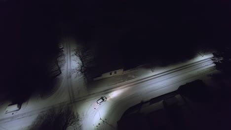 drone follow shot following a white car on a dark night with the streets fully covered with snow on a cold wintry night.