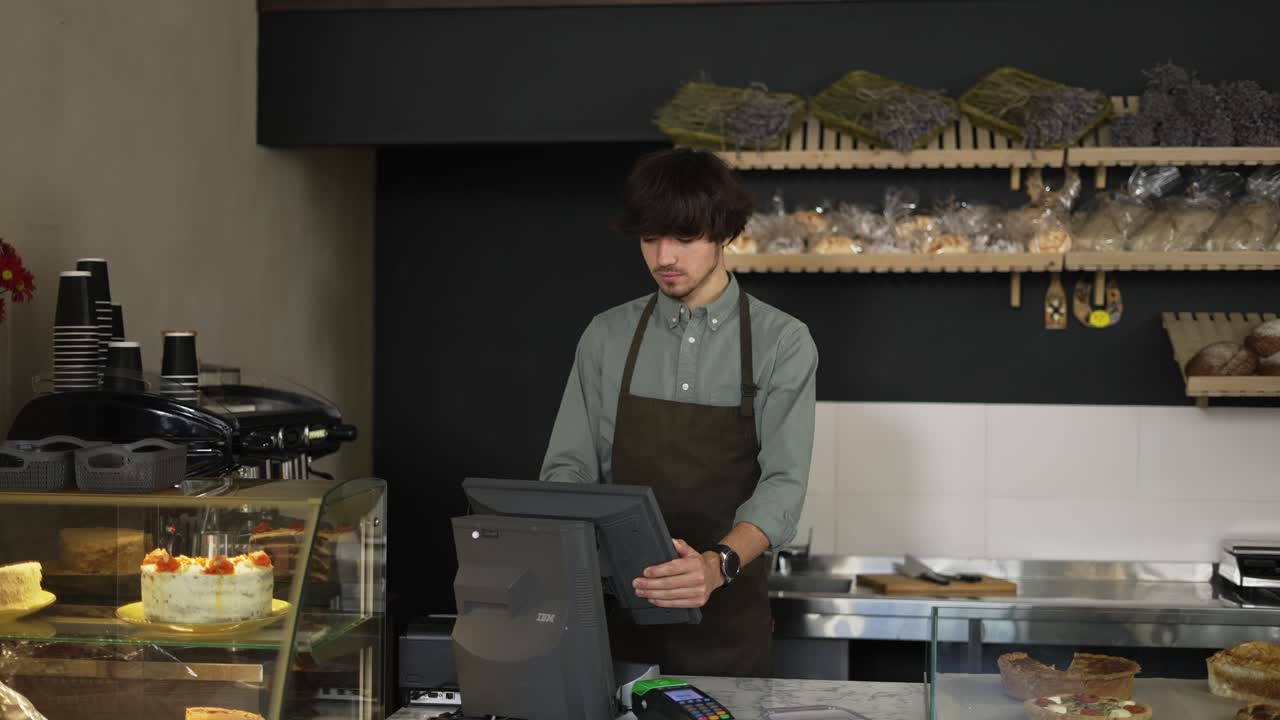 joven cajera en delantal escribiendo en pantalla táctil en una panadería. primer plano, interior, cámara lenta
