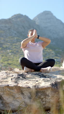 vertical video: meditating in nature, woman sitting cross-legged on rock during mountain hike