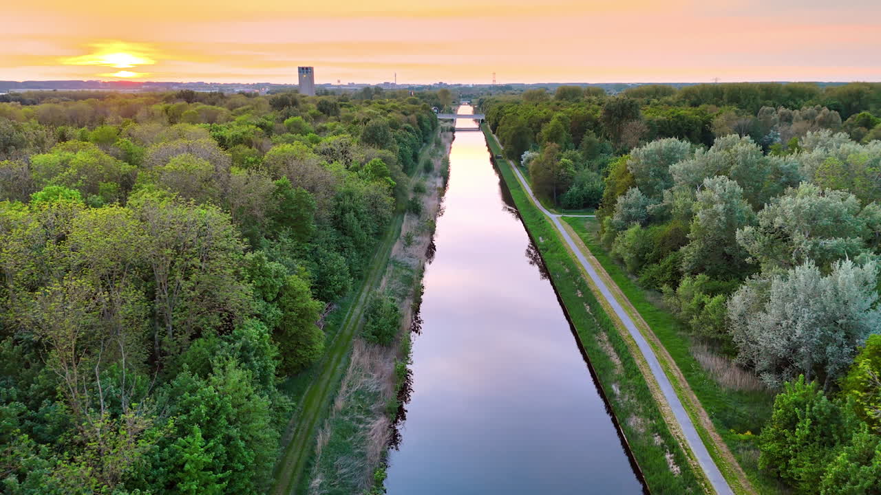 Mirror surface of the canal crossing the forest. Beautiful sky with setting sun at backdrop.