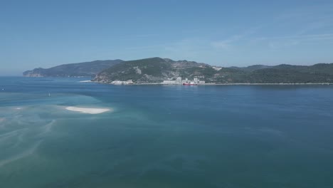 Toma-Aérea-Descendente-De-árboles-En-La-Colina-Frente-Al-Río-Sado-Y-Las-Montañas-Arrabida-En-Portugal