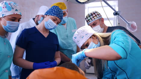 blonde dentistry student is applying metal tools to a patient sitting in the chair. group of colleagues are watching at backdrop.